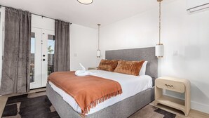 A modern bedroom with a large bed, grey bedding, a brown throw blanket, and a bedside table with a lamp. - Scottsdale Retreat | Pool, Putt & More (Scottsdale)