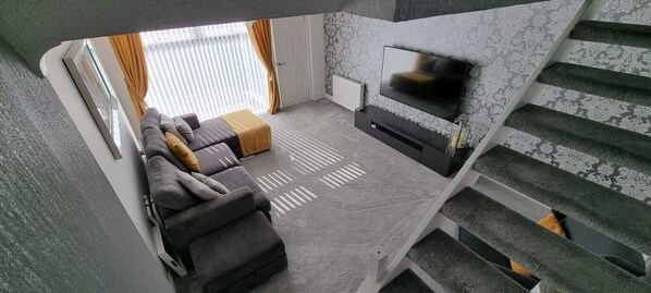 Ein modernes Wohnzimmer mit Sofa, Fernseher und einer Treppe.