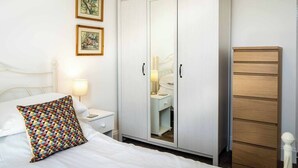 A bedroom with a bed, a wardrobe, a nightstand, and two framed pictures on the wall.