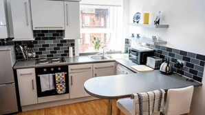 A modern kitchen with white cabinets, a black and white tiled backsplash, a window, and a small dining area with a table and chairs.