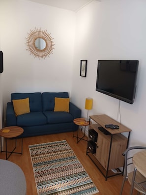 A living room with a blue sofa, a TV, a small wooden table, and a patterned rug.