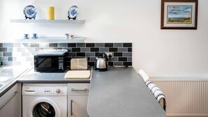 A compact kitchen with a washing machine, microwave, toaster, kettle, and a countertop with a towel.