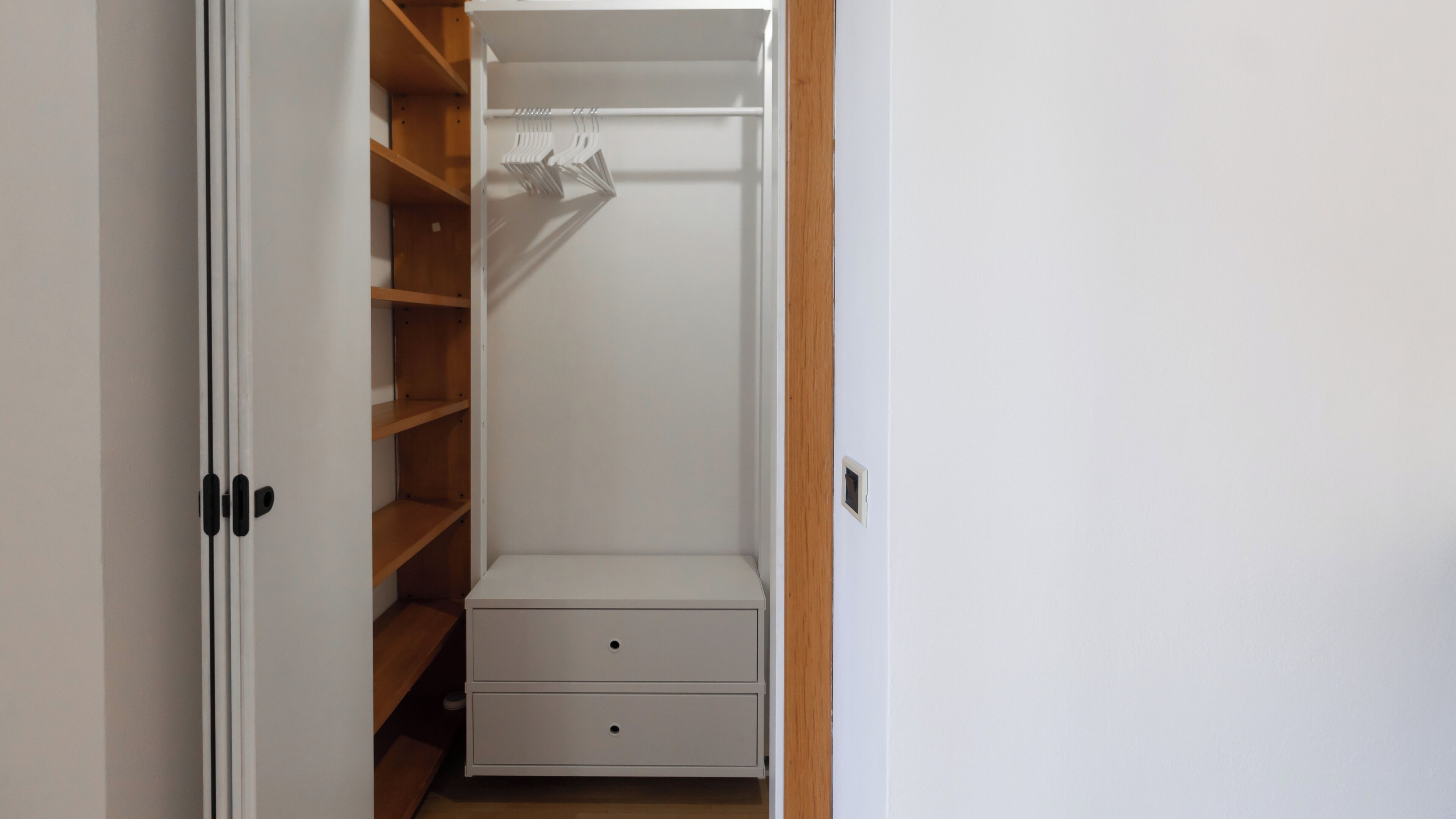 A walk-in closet with wooden shelves, a hanging rod, and two drawers.