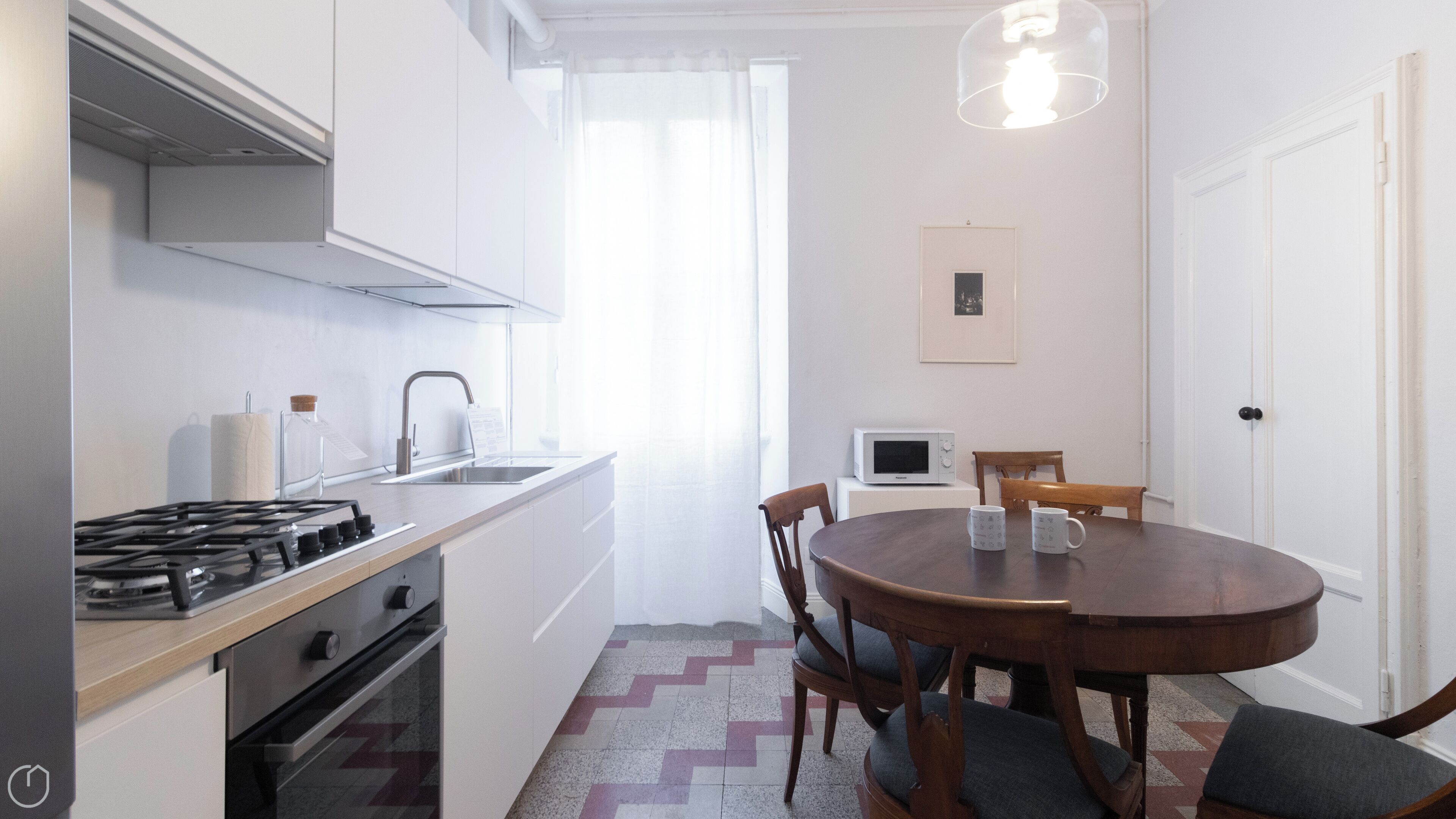 Une cuisine compacte équipée d’une cuisinière à gaz, d’un évier et d’un four à micro-ondes. On y trouve une table à manger avec des chaises et un luminaire suspendu.