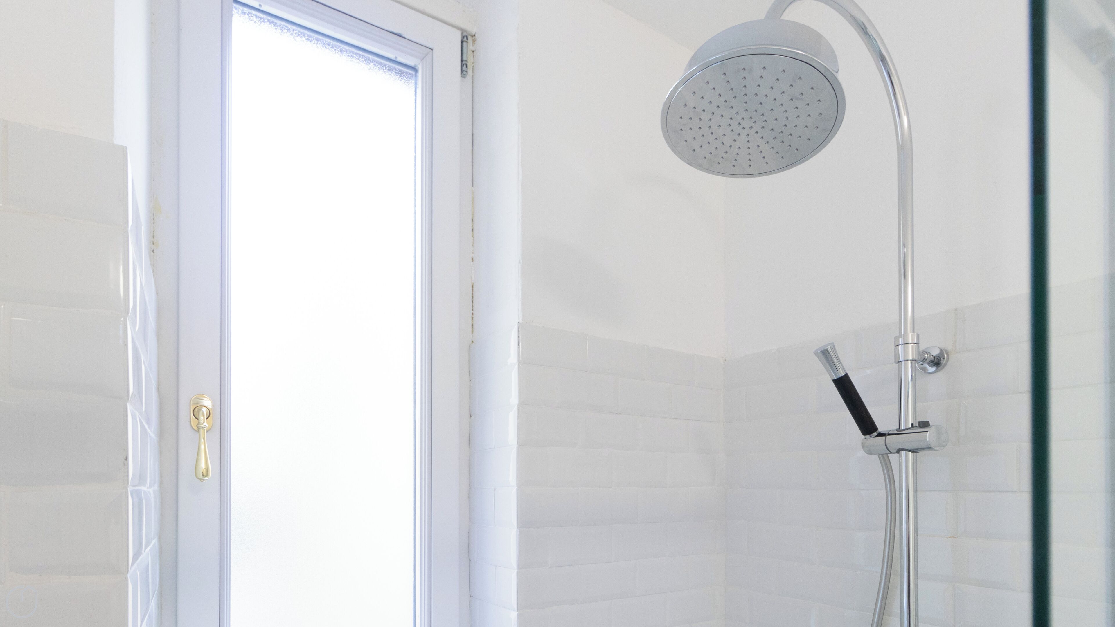A modern bathroom with a shower, white tiled walls, and a door with a golden handle.