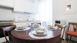 Une cuisine moderne avec des meubles blancs, une table à manger dressée avec des assiettes, des bols et des verres, et un four à micro-ondes posé sur le plan de travail.
