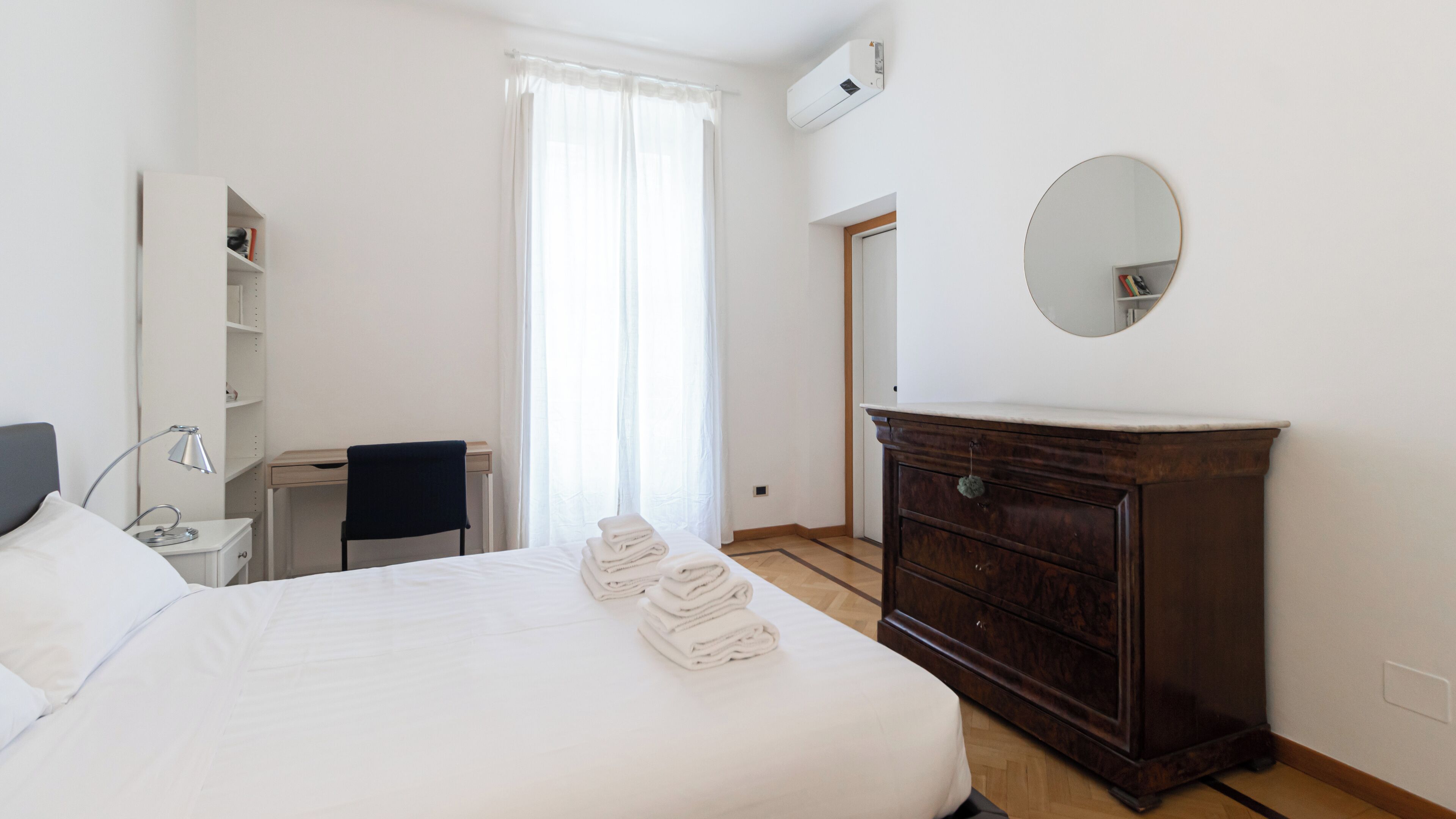 A hotel room with a bed, a desk, a chair, a dresser, and a mirror.
