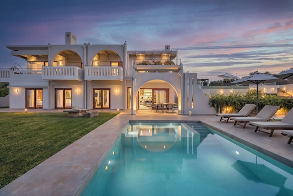 A modern two-story house with a swimming pool, outdoor seating, and a well-lit entrance.