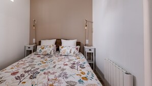 Ein Schlafzimmer mit blumigem Bettbezug, einer Lampenschirm aus Weidengeflecht, einem weißen Heizkörper und zwei Nachttischen mit Lampen.