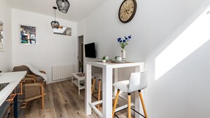 Eine moderne Küche mit weißen Schränken, ein Essbereich mit Holzkästen, einem weißen Tisch und einem an der Wand befestigten Fernseher.