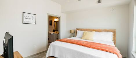 A bedroom with a bed, a ceiling fan, a TV on a wooden stand, and a framed sign on the wall.