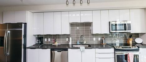 A modern kitchen with stainless steel appliances, white cabinets, and a black countertop.