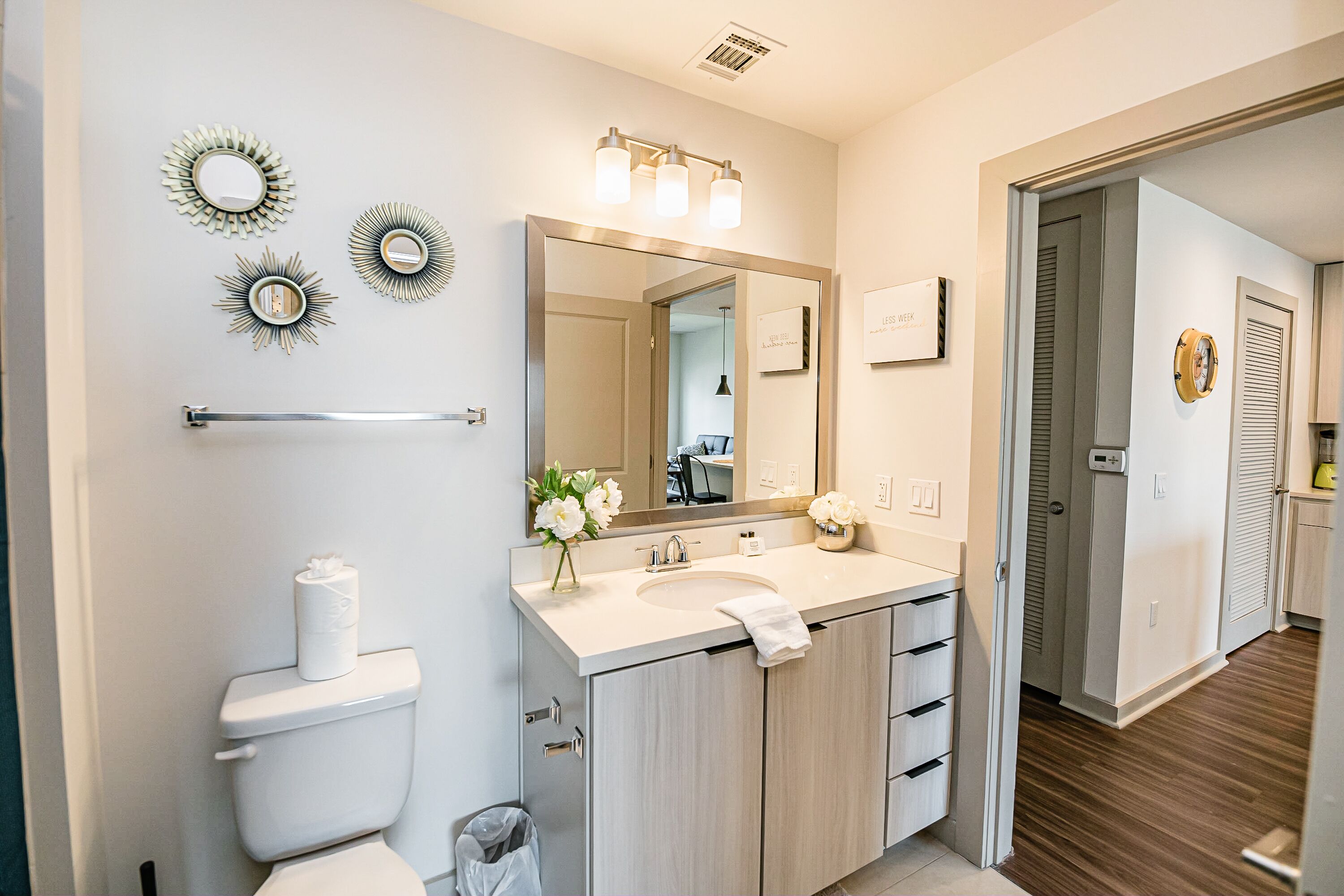 A modern bathroom with a toilet, sink, and mirror. There are decorative wall mirrors and a towel rack.
