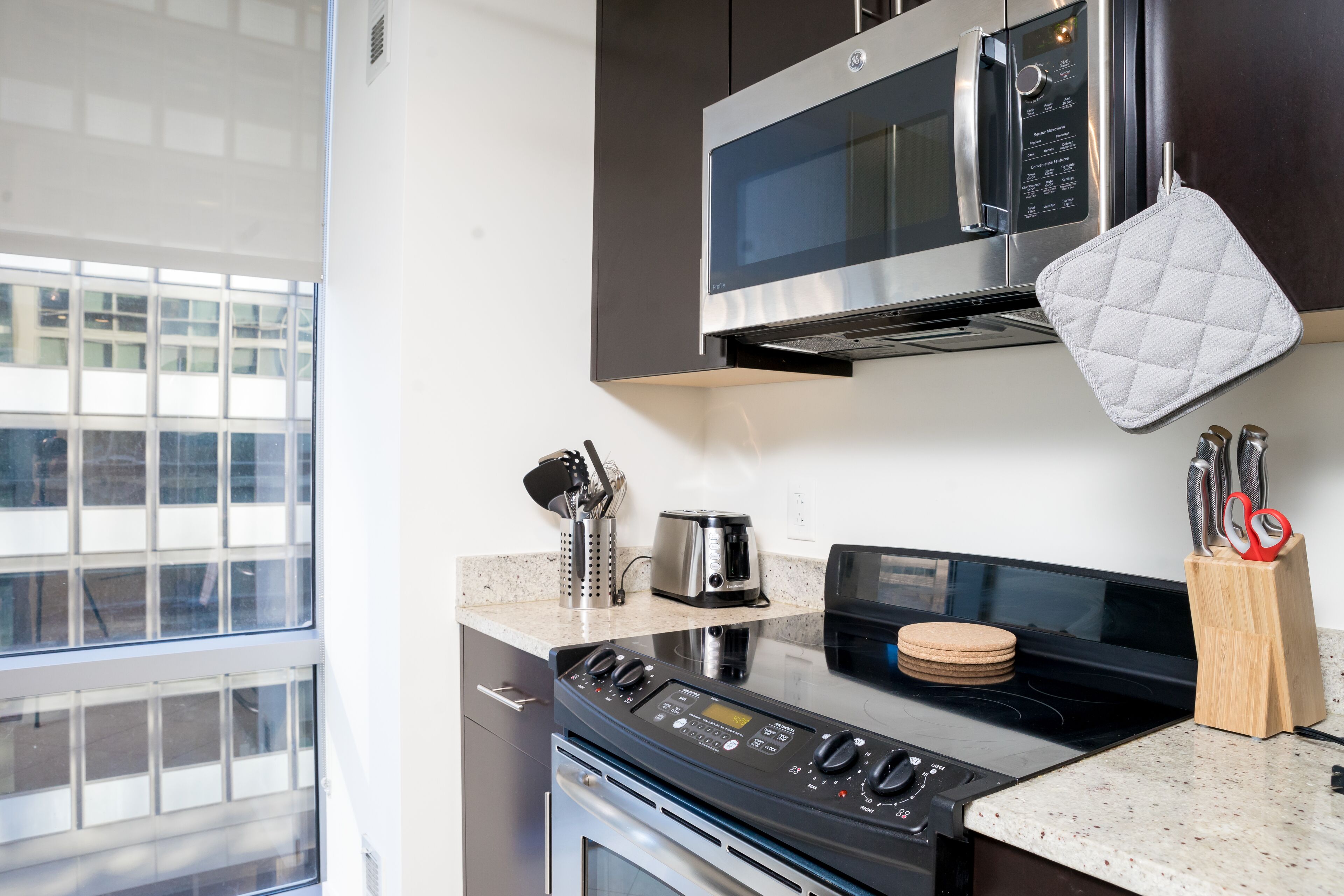 A modern kitchen with a stainless steel microwave, oven, and stove, a granite countertop, and a window providing a view of the cityscape.