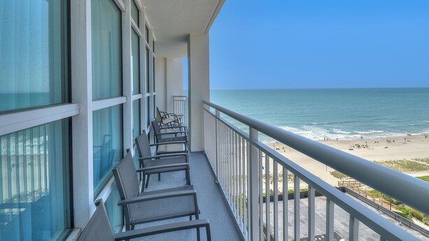 A balcony with a view of the beach, featuring a railing and several chairs.