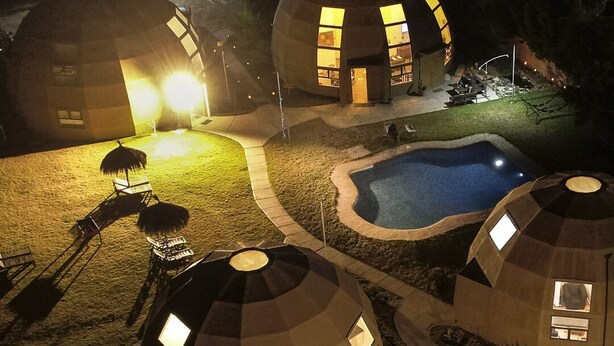 Un conjunto de estructuras en forma de cúpulas geodésicas con ventanas, una piscina y mobiliario exterior.