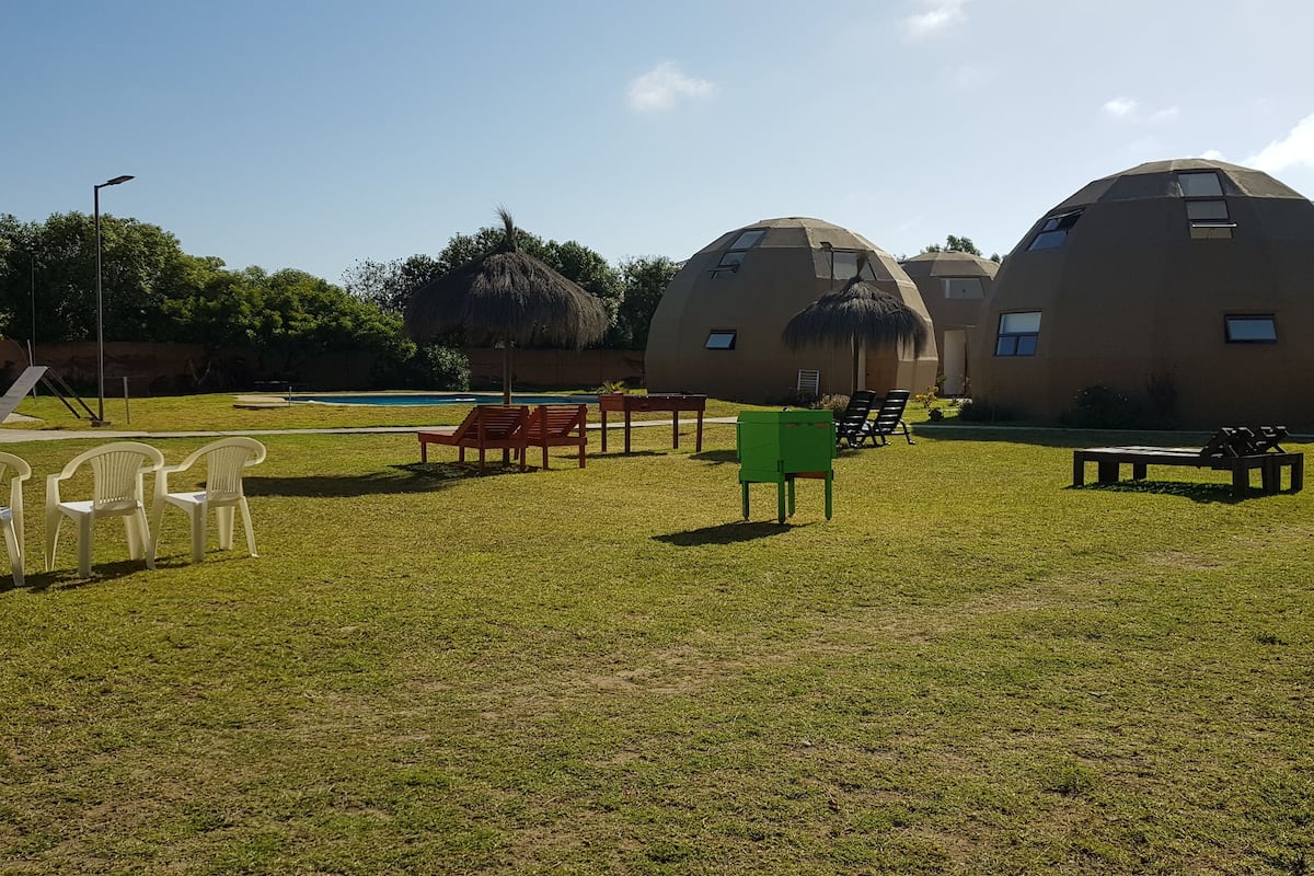 A grassy area with several dome-shaped buildings, outdoor seating, and a pool in the background.