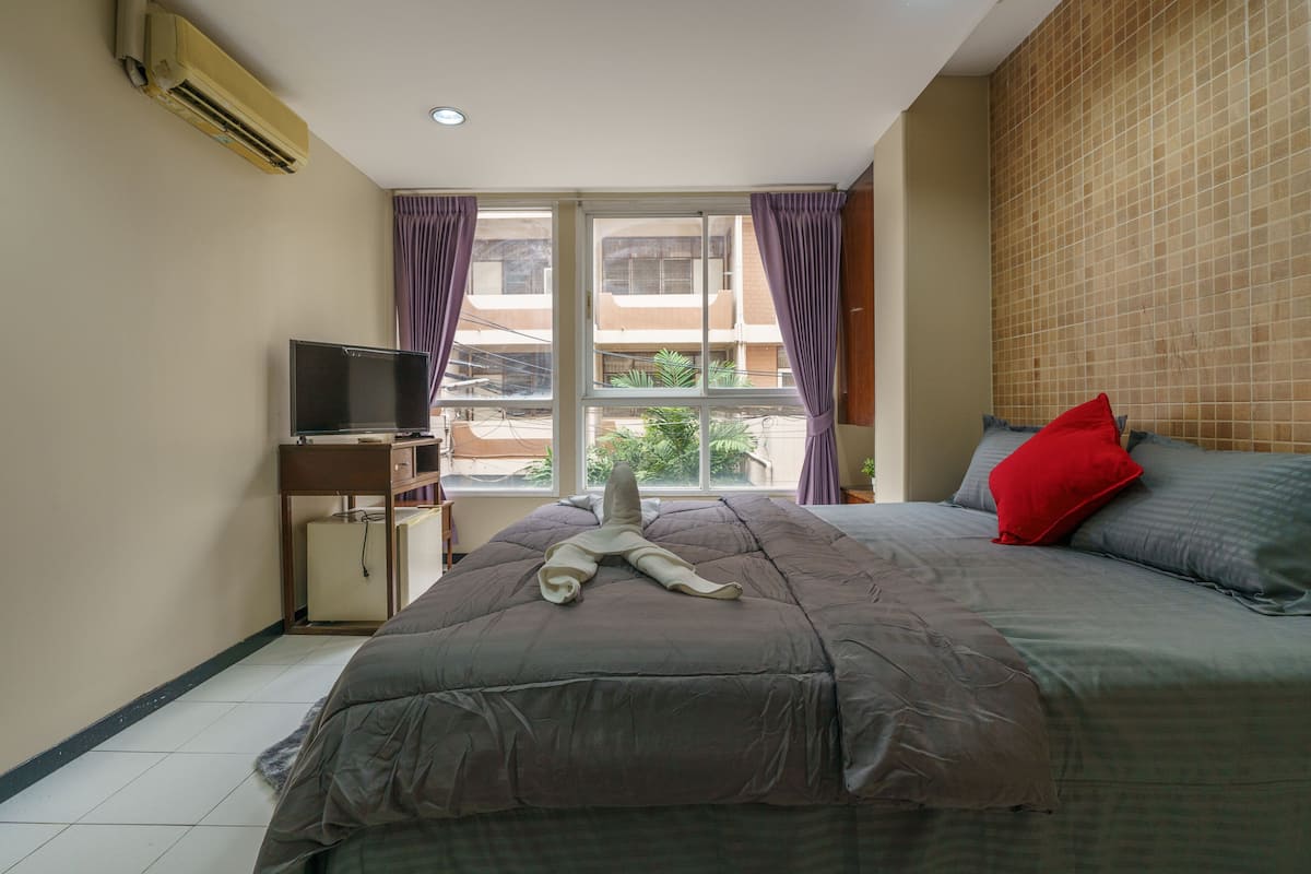 A bedroom with a bed, a TV on a stand, and a window with curtains.
