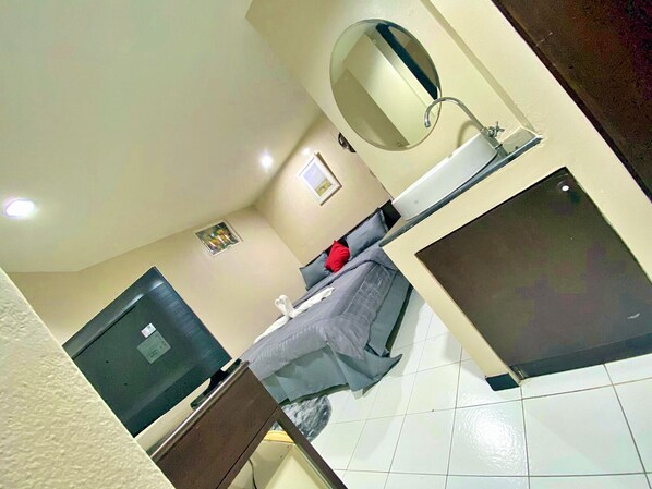 A hotel room with a bed, a bedside table, a mirror, a window, and a television. -  Sukhumvit Beds (Bangkok)
