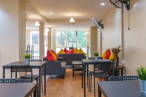 A modern living room with a grey sofa, black chairs, and a dining table. There are potted plants and a large window with a view of greenery. -  Sukhumvit Beds (Bangkok)