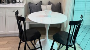 A modern kitchen with white cabinets, a round white table with two black chairs, a hanging light fixture, and a framed picture of a pool on the wall. - Casa Marina Cottage+ private pool+walk to Duvall st. (Key West)
