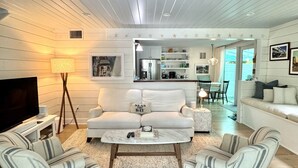 A modern living room with a white sofa, striped armchairs, a coffee table, and a TV. - Casa Marina Cottage+ private pool+walk to Duvall st. (Key West)
