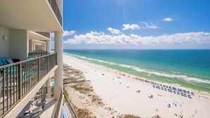 A beachfront hotel balcony with lounge chairs and umbrellas, a sandy beach, and the ocean.