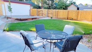 Eine Terrasse mit rundem Tisch und vier Stühlen, umgeben von einem Holzzaun und einem Rasen.