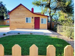 Standalone cabin with a red door and white-framed windows, set amidst a well-maintained lawn and wooden picket fence.