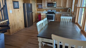 L’intérieur d’une cabane en bois comprend un coin cuisine équipé d’un réfrigérateur, d’un four à micro-ondes, d’une cuisinière et d’un évier. On y trouve également une table à manger avec des chaises et un escalier menant à un autre niveau.