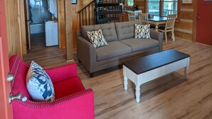 Un intérieur en bois comprenant un espace de vie, un canapé rouge, un canapé gris, une table à manger et un escalier en colimaçon.