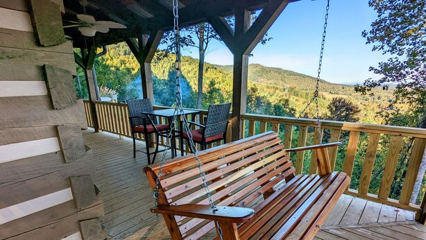 Une terrasse en bois avec un banc et des chaises, offrant une vue sur un paysage vallonné.