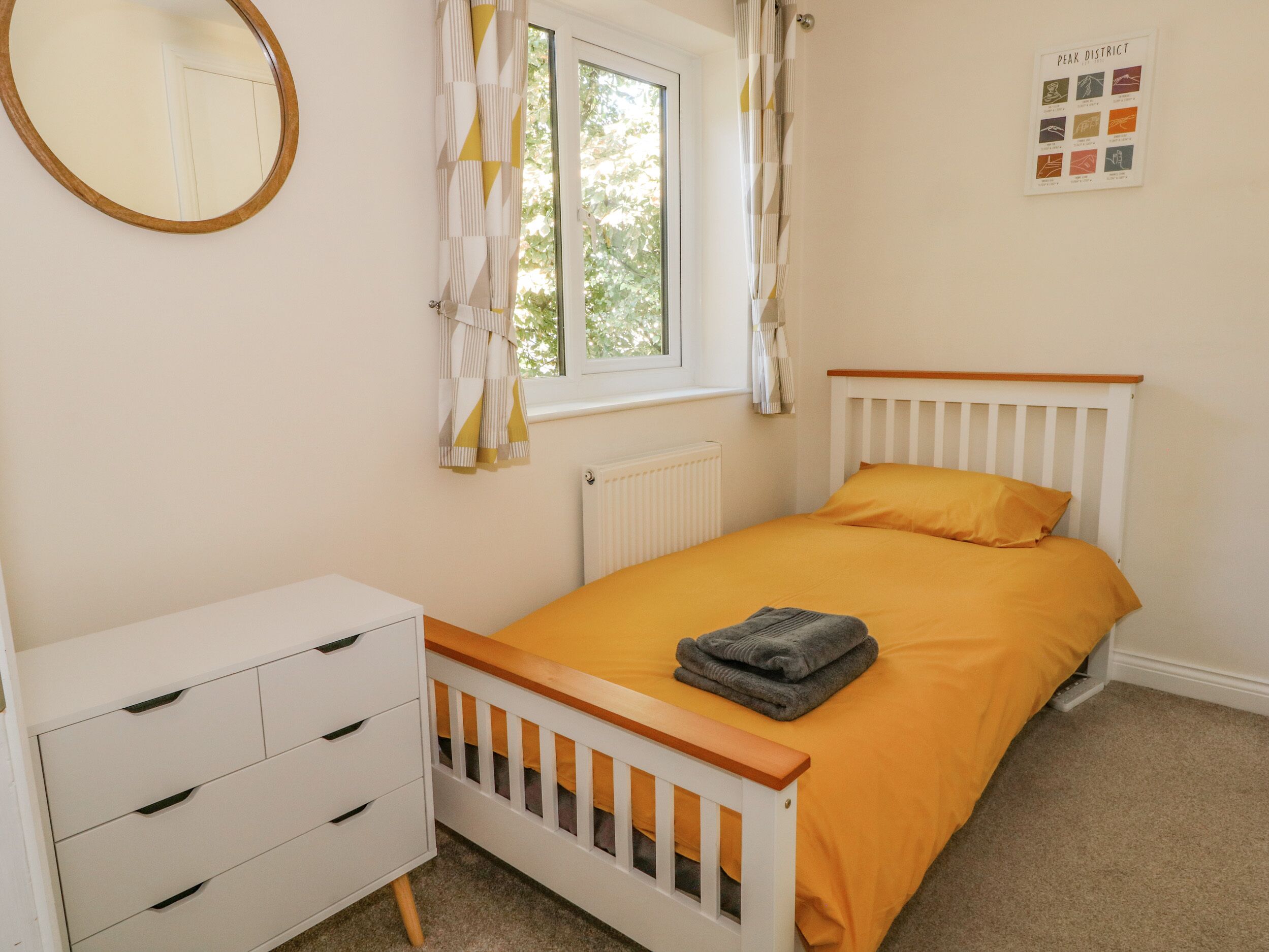 Un dormitorio con cama, cómoda, ventana con cortinas y espejo montado en la pared.