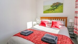 Een net opgemaakt bed met een rood-grijs dekbed, twee kussens en twee opgevouwen handdoeken.