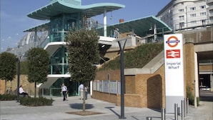 A modern building with a glass facade and a sign for 'Imperial Wharf' with a train station logo.
