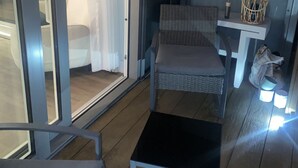 A small, enclosed balcony area with a wicker chair, a small table, and a wicker basket.