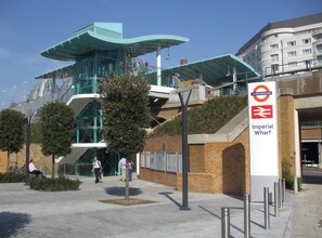 A modern building with a glass facade and a sign for 'Imperial Wharf' with a train station logo.