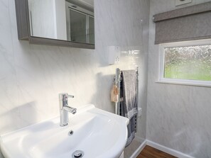 Un baño con lavamanos blanco, un espejo, toallero y ventana con vista a zonas verdes.
