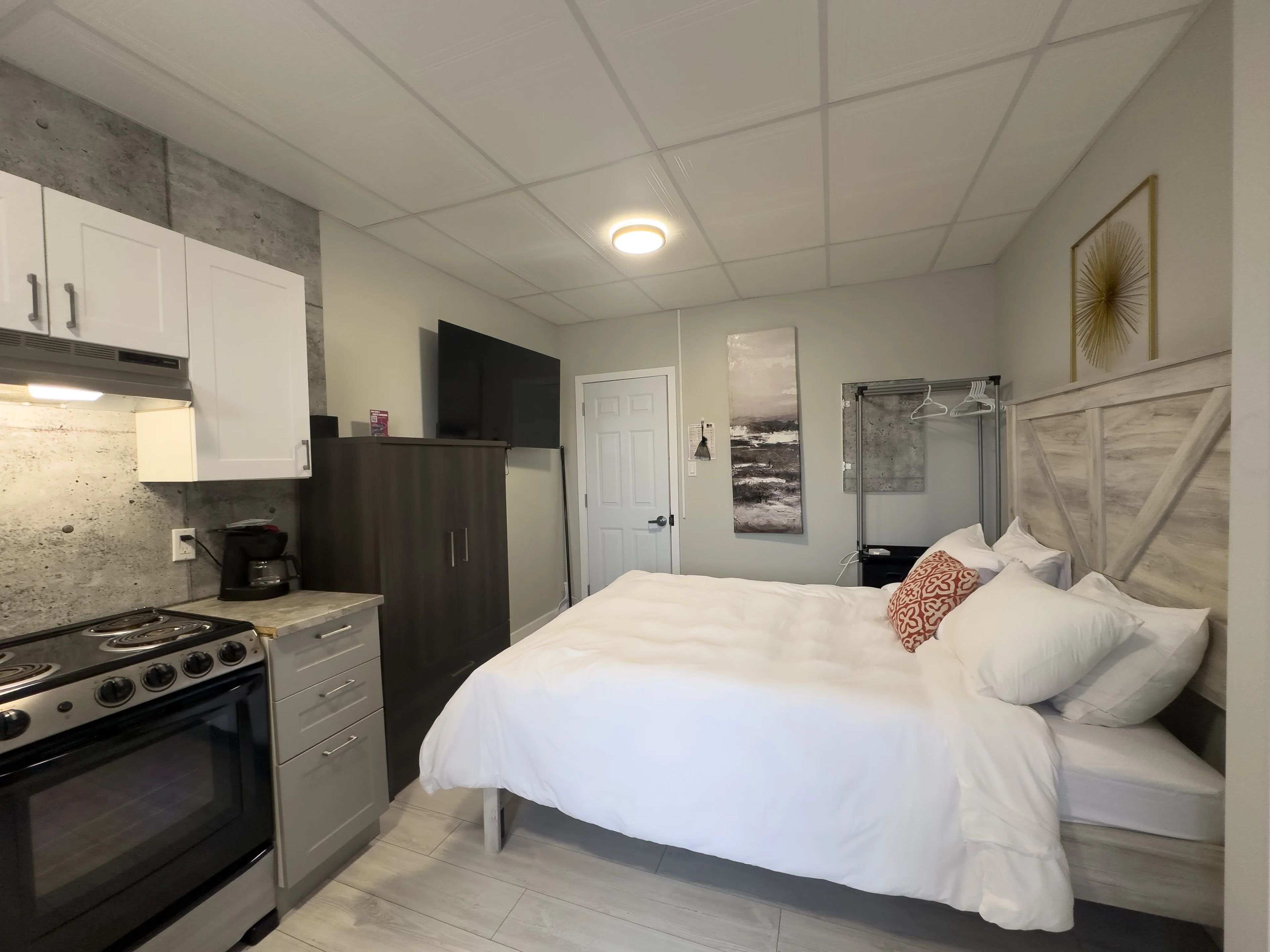 Une chambre à coucher comprenant un lit, une commode, une table de chevet et un téléviseur fixé au mur.