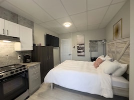 Un dormitorio con cama, cómoda, mesita de noche y televisión montada en la pared.