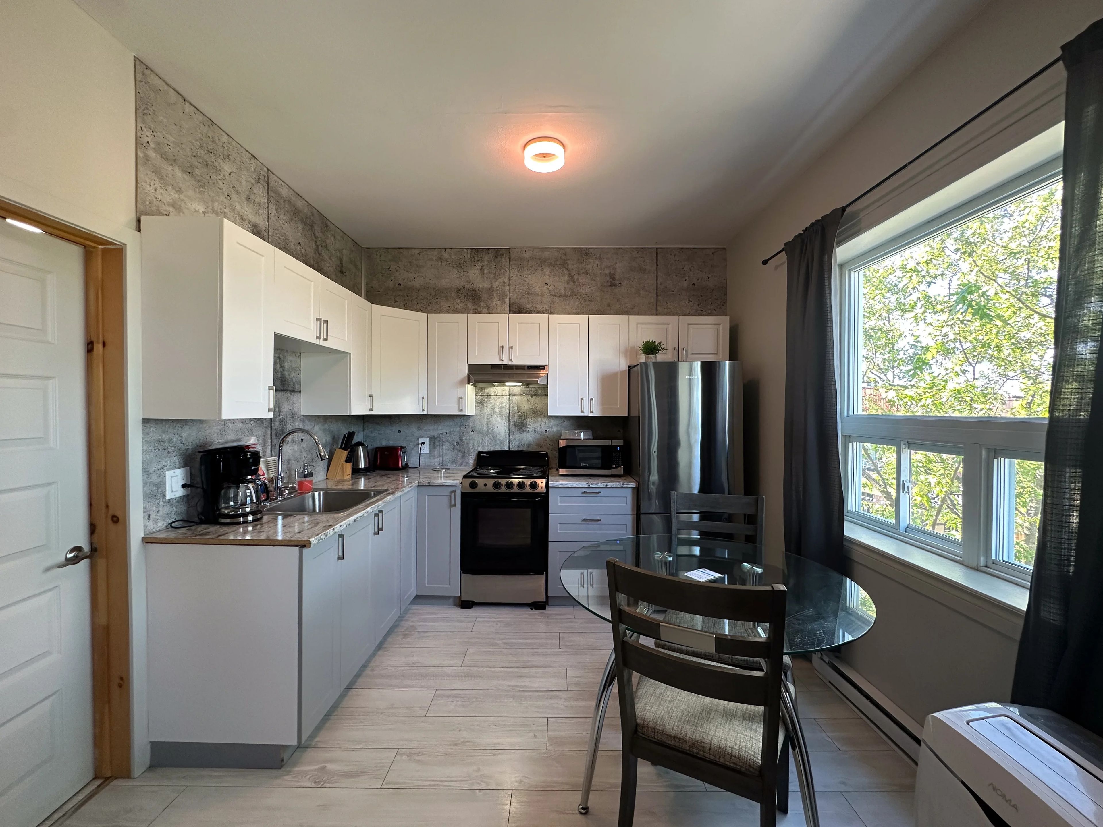 A modern kitchen with white cabinets, a stainless steel refrigerator, a stove, and a dining area with a glass table and chairs.