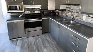 A modern kitchen with stainless steel appliances, grey cabinetry, and a tiled backsplash. - Le Convivial (Rouyn-Noranda)