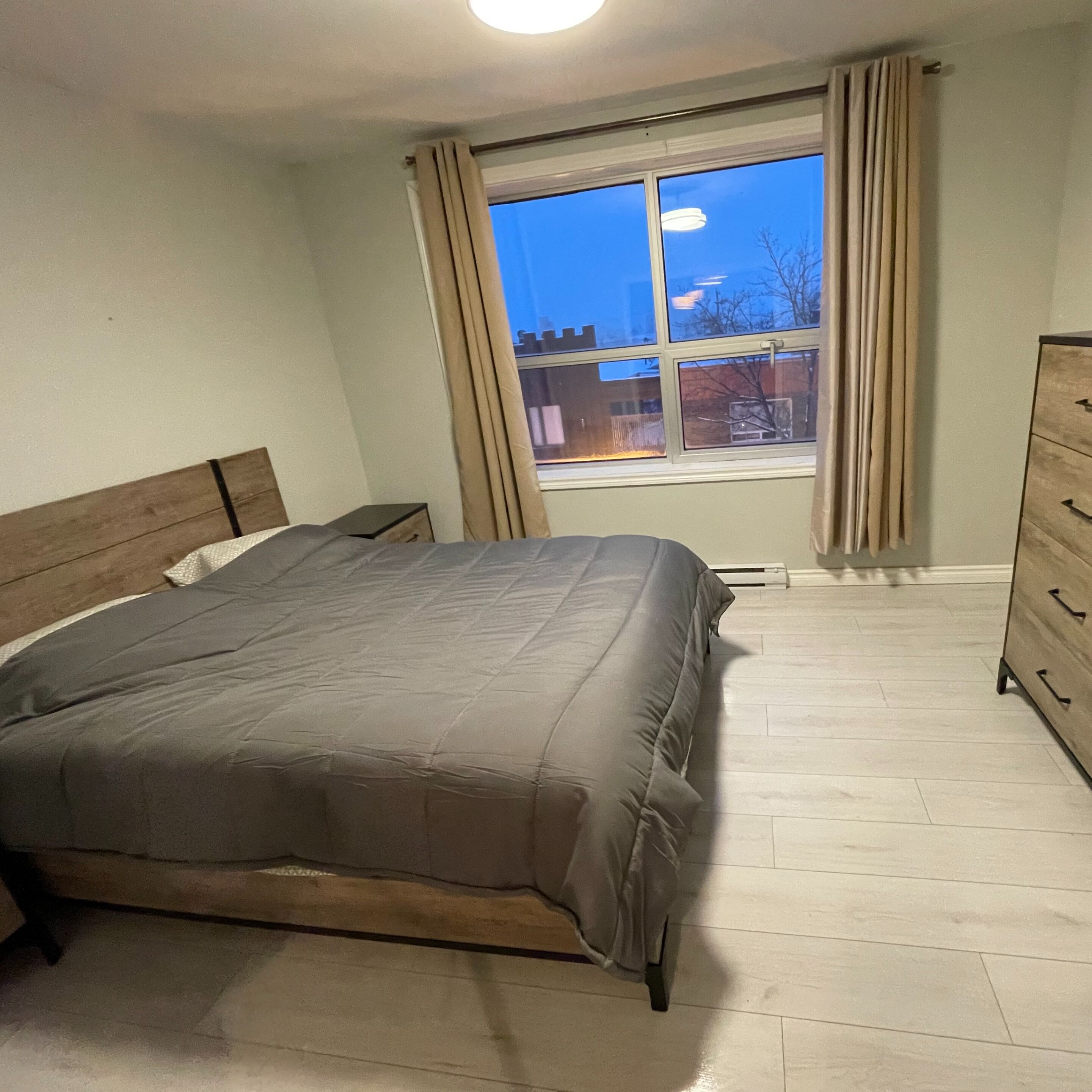 A bedroom with a bed, a dresser, and a window with curtains.