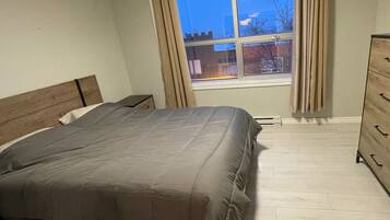 A bedroom with a bed, a dresser, and a window with curtains.