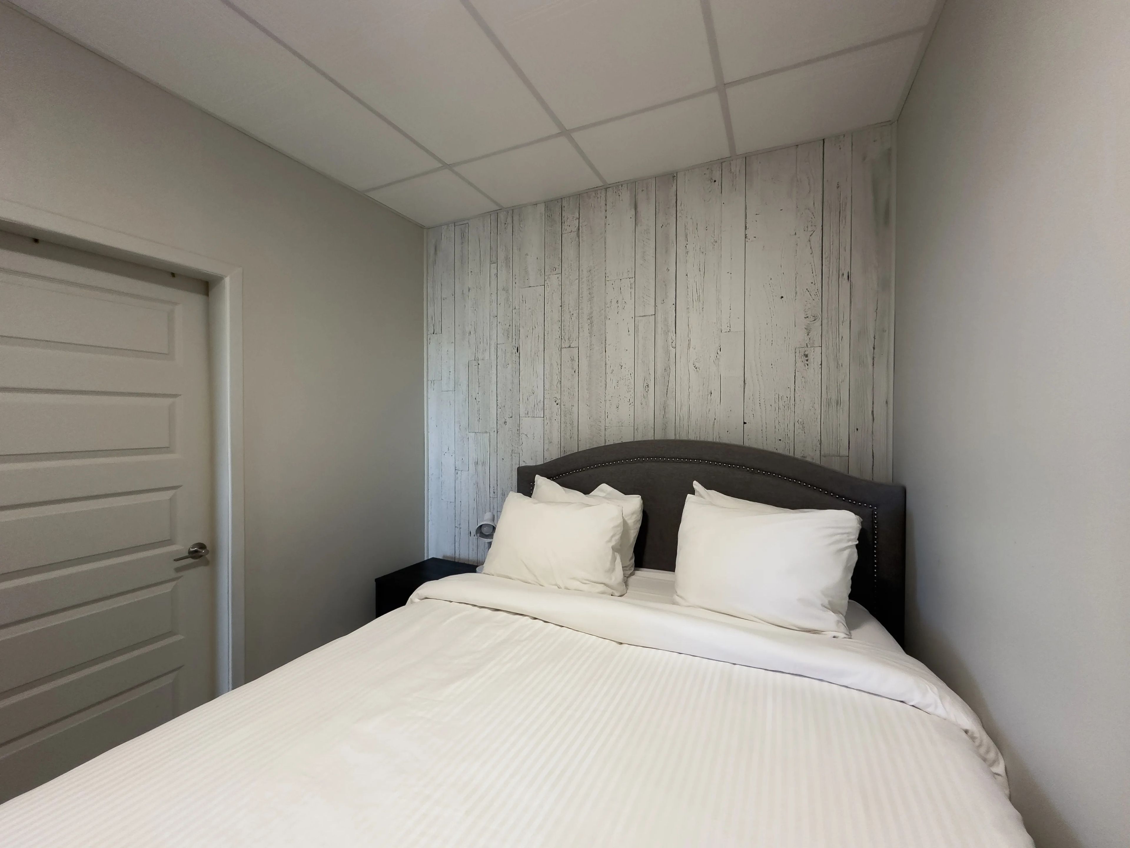 A bedroom with a bed, a nightstand, a door, and a wall with a wooden panel design.