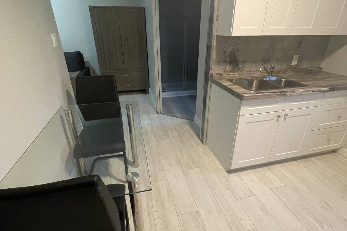 A kitchen with white cabinets, a stainless steel sink, and a wooden floor.
