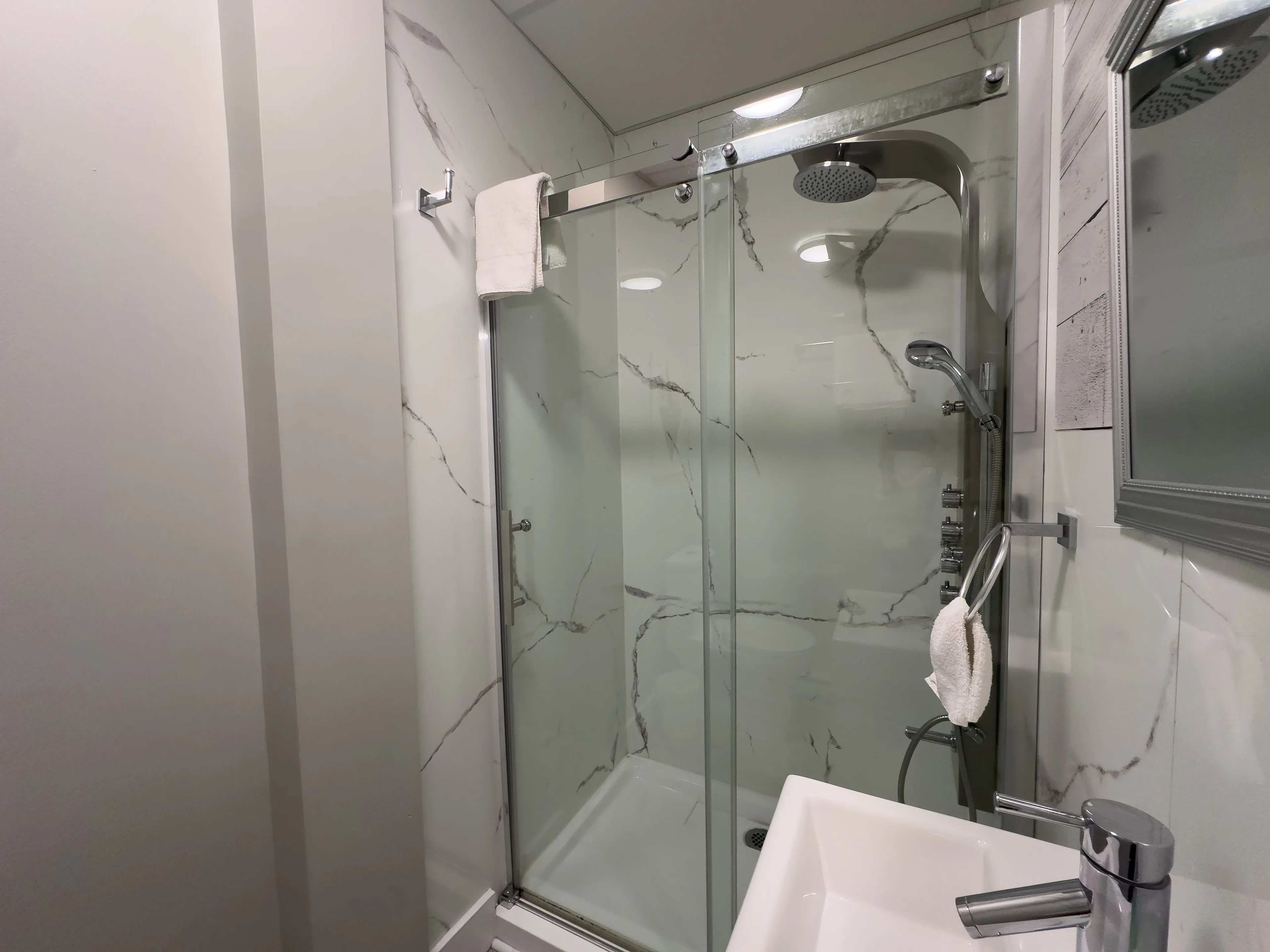 A modern bathroom with a glass-enclosed shower, a white sink, and a mirror.