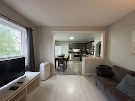 Una sala de estar con una televisión de pantalla plana, un mini refrigerador blanco y un sofá con un cojín mullido.