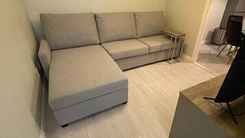 Una sala de estar moderna con un sofá seccional gris, una mesita auxiliar y suelo de madera.
