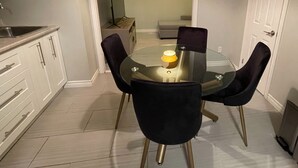 A compact kitchen with white cabinets, a sink, and a dining area with a glass table and four chairs. - Le Convivial (Rouyn-Noranda)